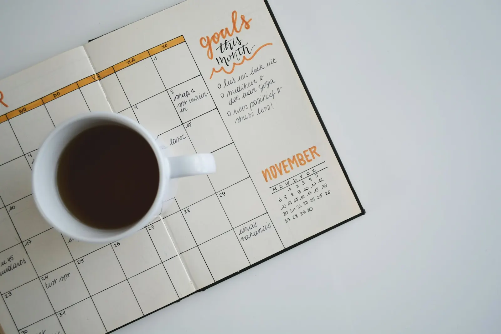 Agenda ouvert sur un planning mensuel écrit à la main, avec une tasse de café posée dessus