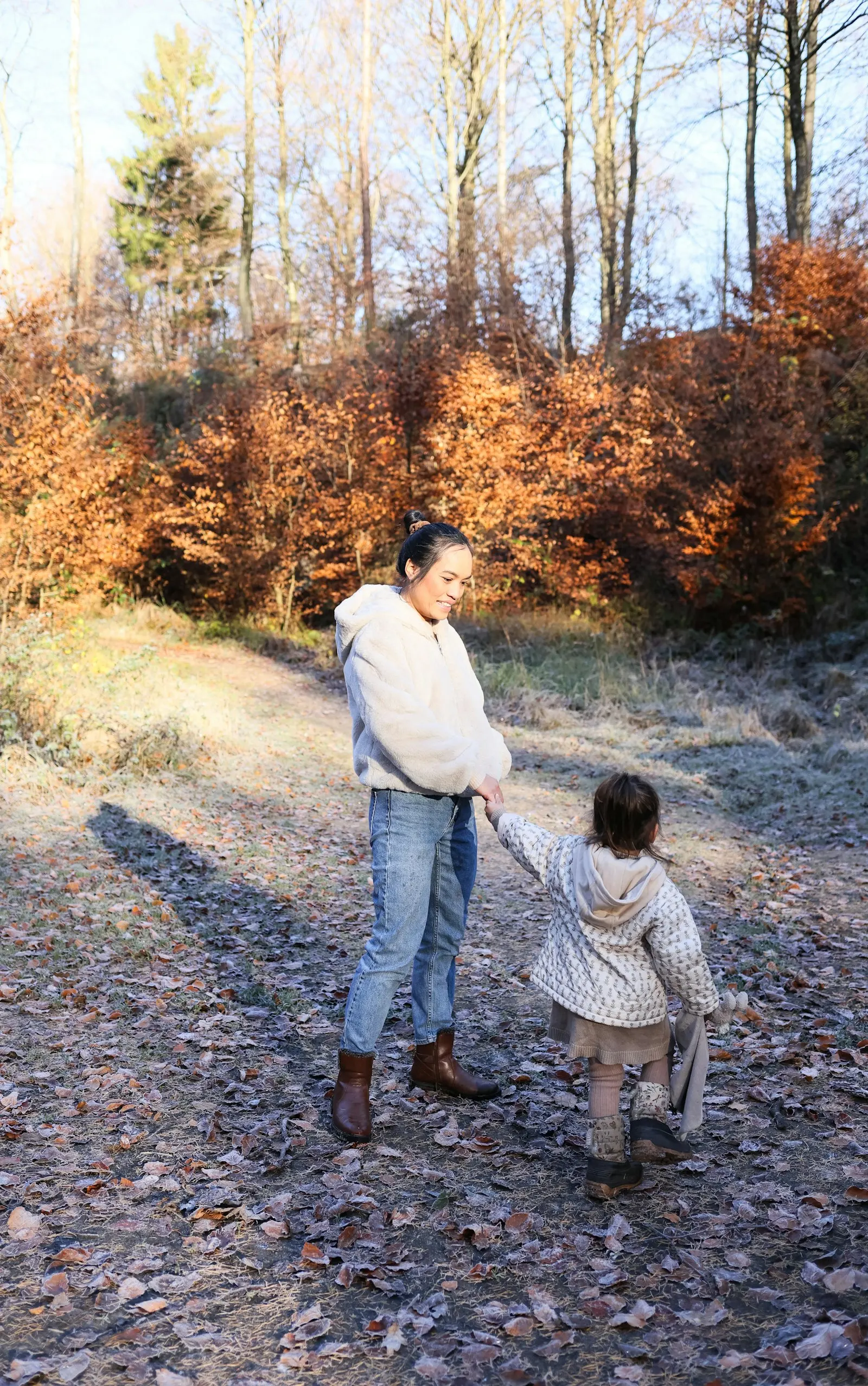Une femme et un enfant marchent main dans la main sur un sentier forestier en automne
