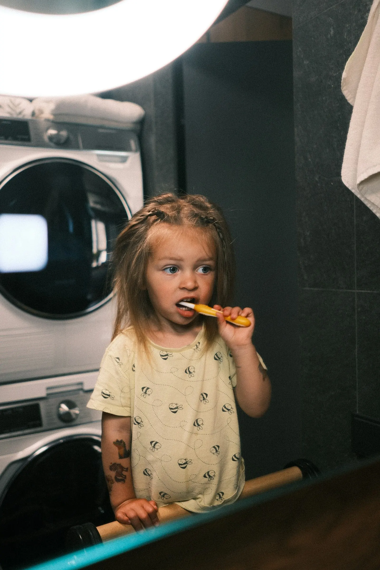 Une petite fille se brosse les dents devant le miroir de la salle de bain