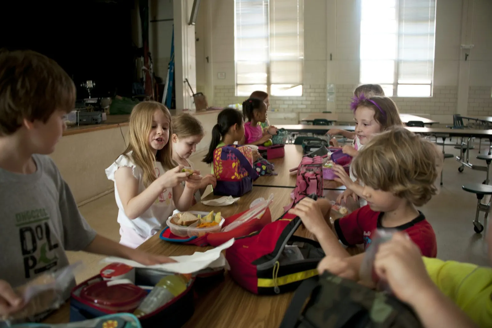 Des enfants déjeunent ensemble à une grande table dans une salle de cantine