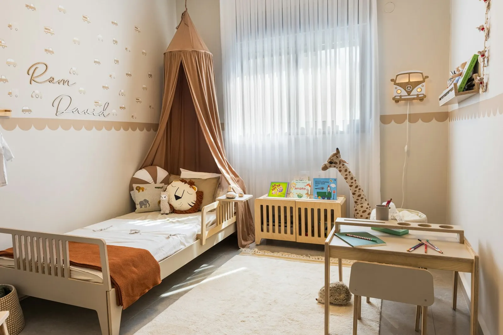 Une chambre d'enfant aux tons clairs avec un lit en bois, un ciel de lit, un petit bureau et des peluches