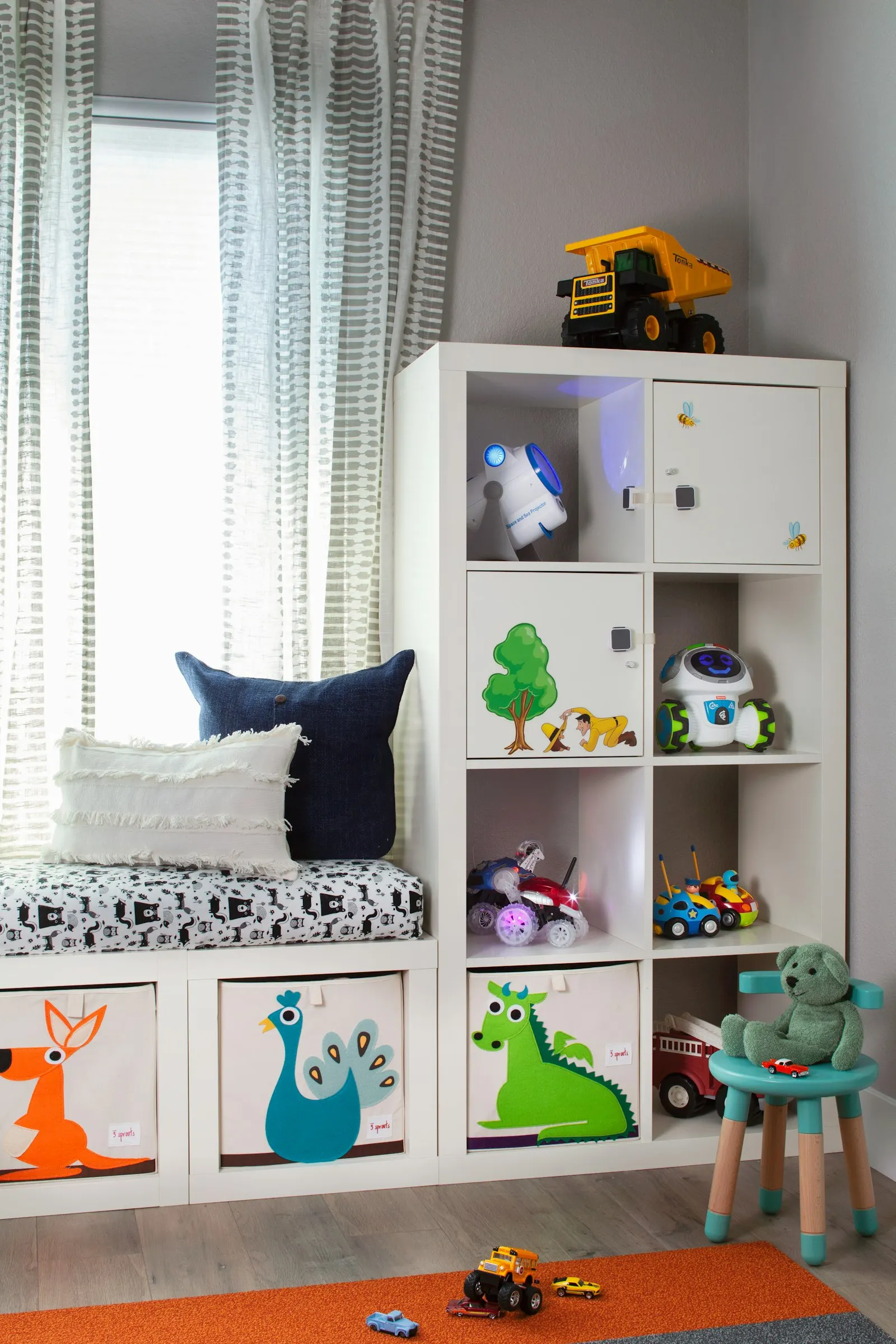 Une chambre d'enfant avec une étagère à casiers, des bacs de rangement décorés et une banquette sous la fenêtre