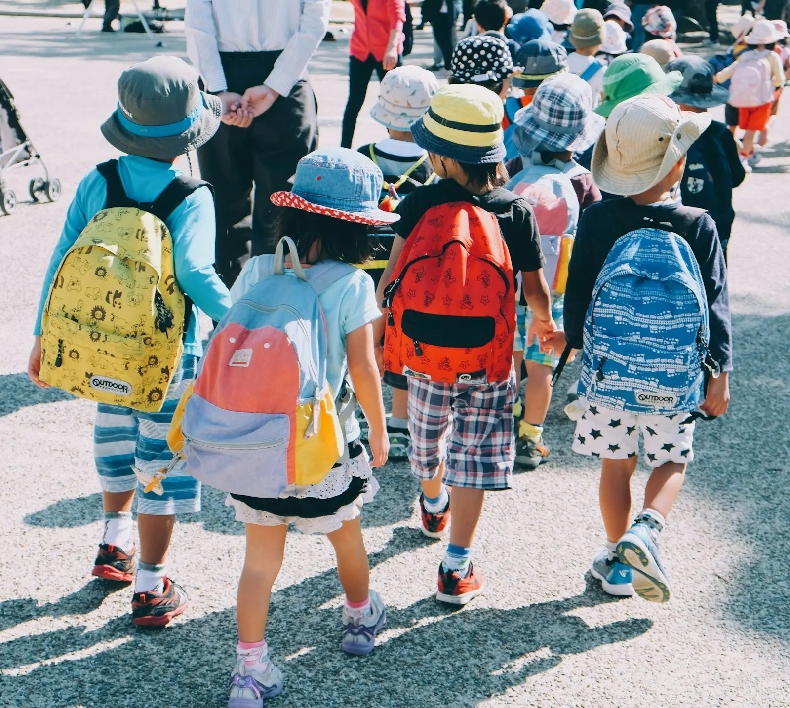 Des jeunes enfants avec chapeaux et cartables marchent ensemble sur un trottoir