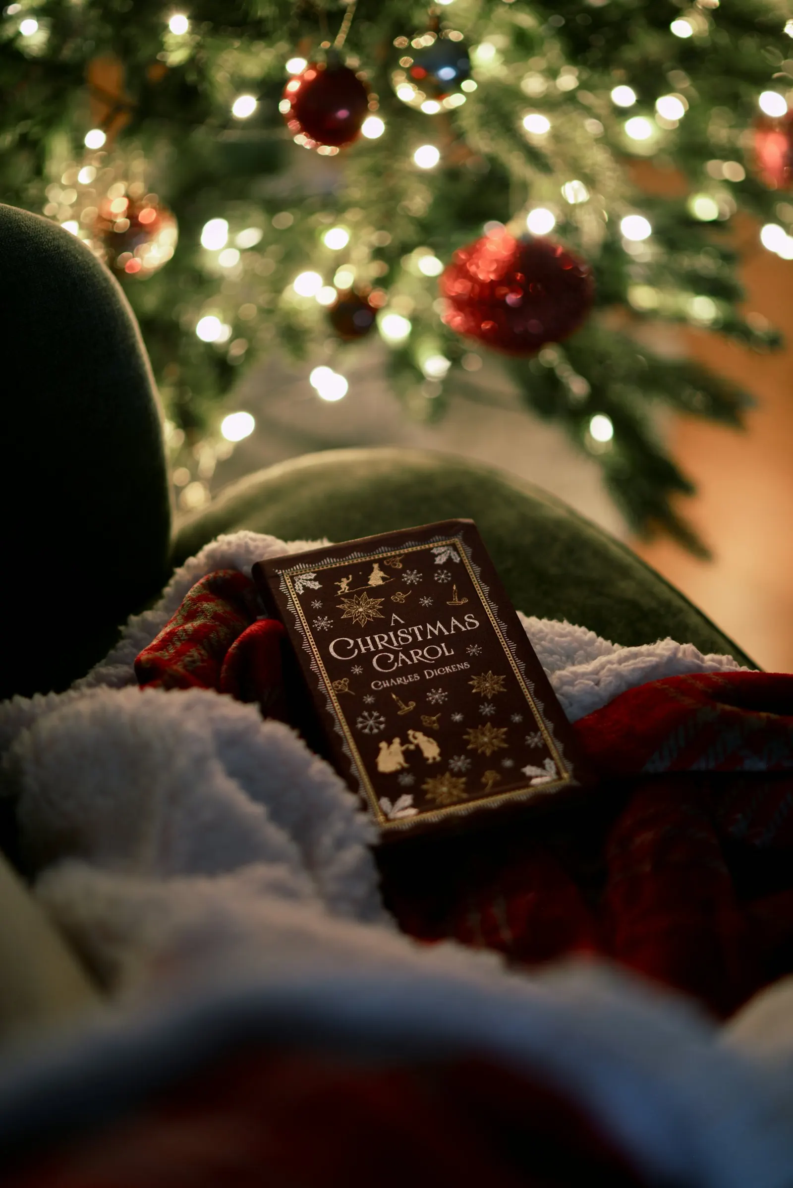 Un livre « A Christmas Carol » de Charles Dickens posé sur une couverture rouge devant un sapin illuminé