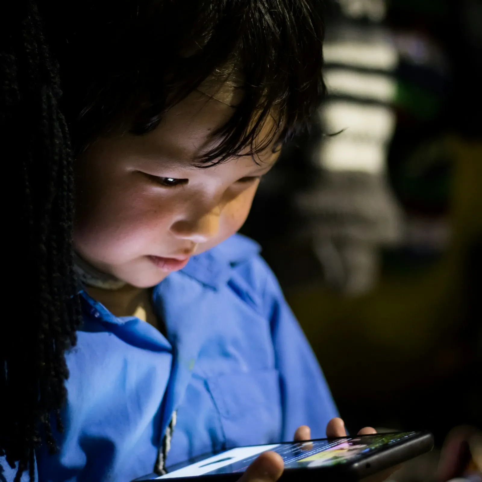 Un jeune enfant regarde un téléphone dans la pénombre