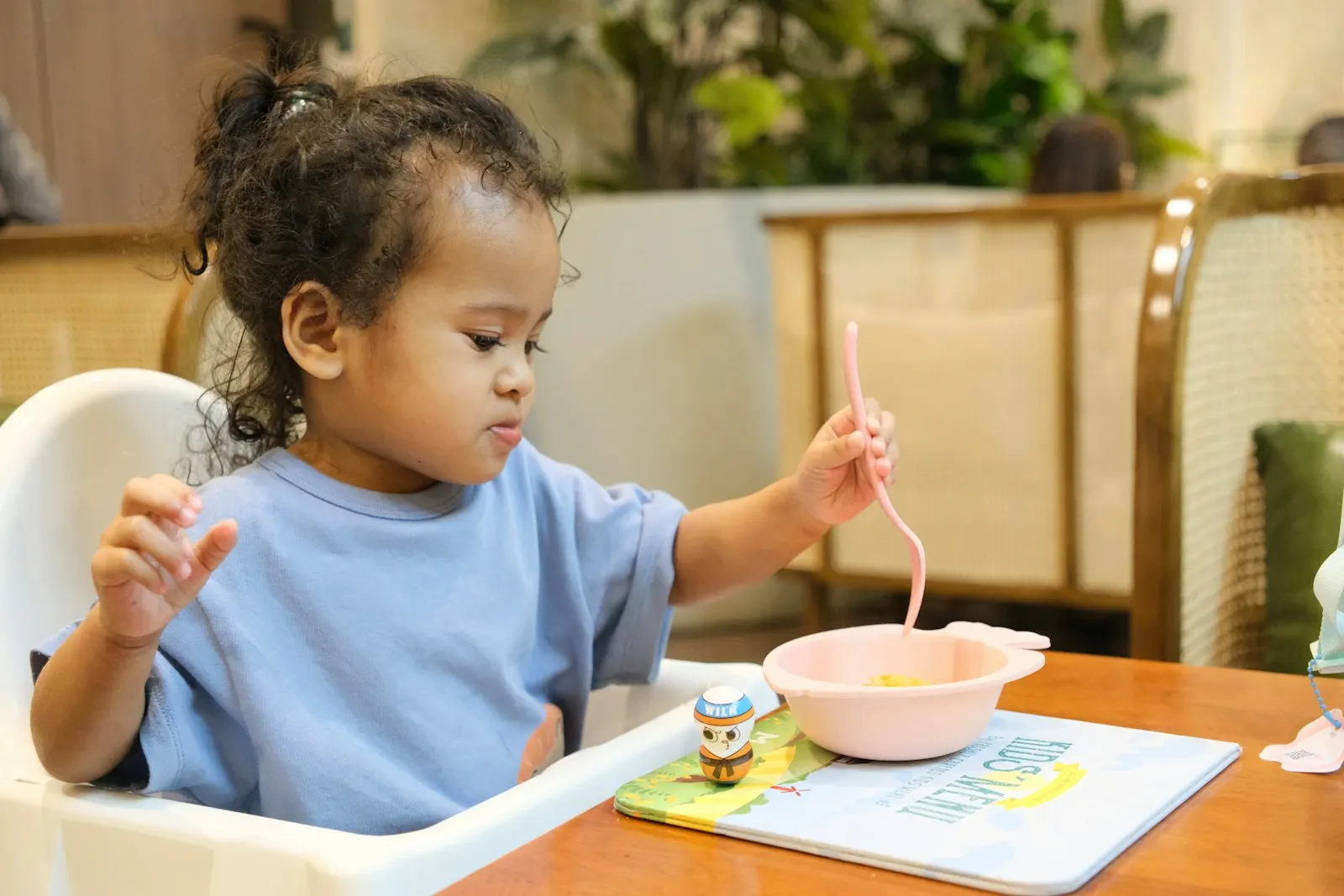 Une petite fille dans une chaise haute mange avec une cuillère rose dans un bol