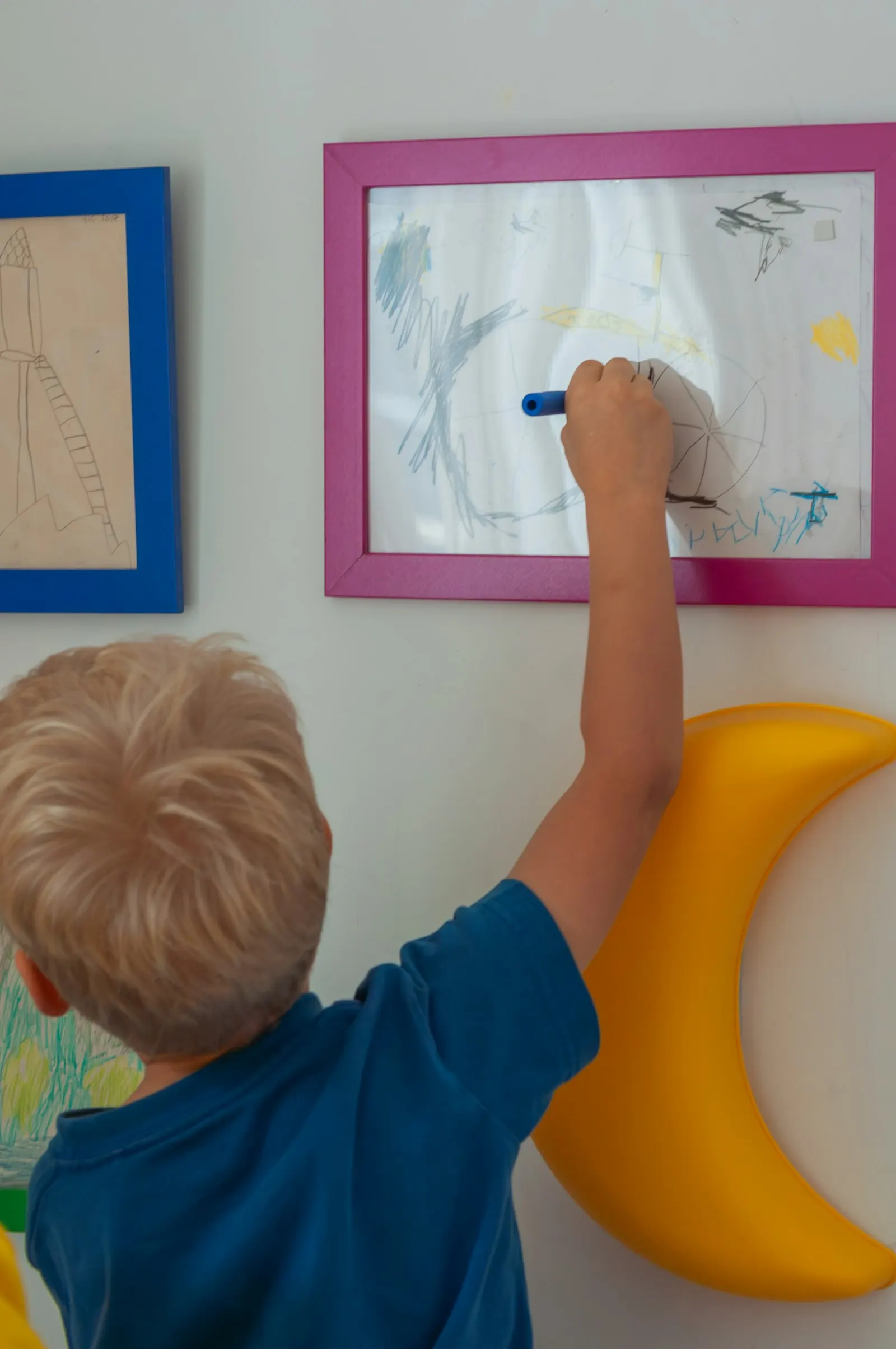 Un petit garçon dessine au feutre sur un tableau accroché au mur