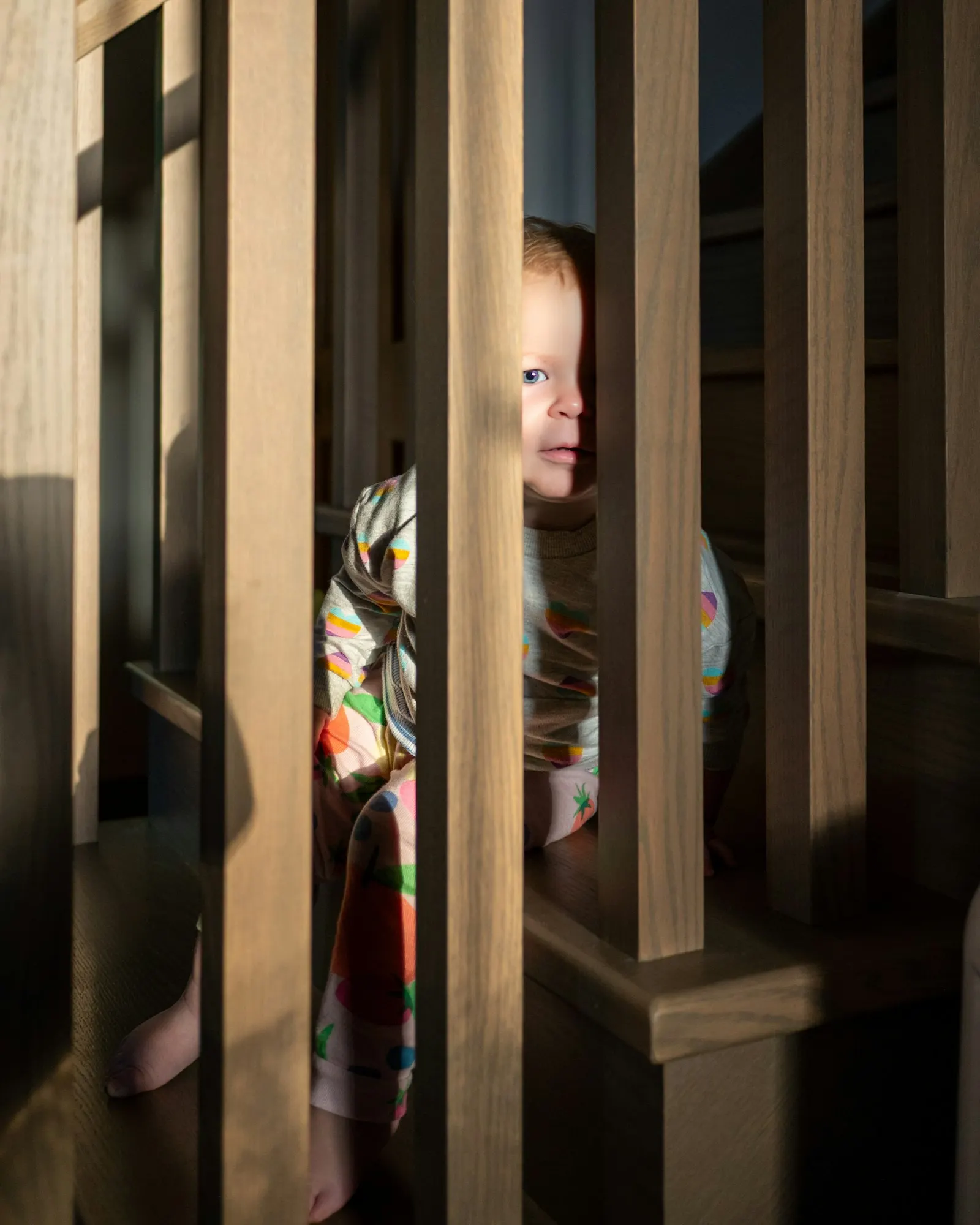 Un jeune enfant en pyjama regarde entre les barreaux en bois d'un escalier