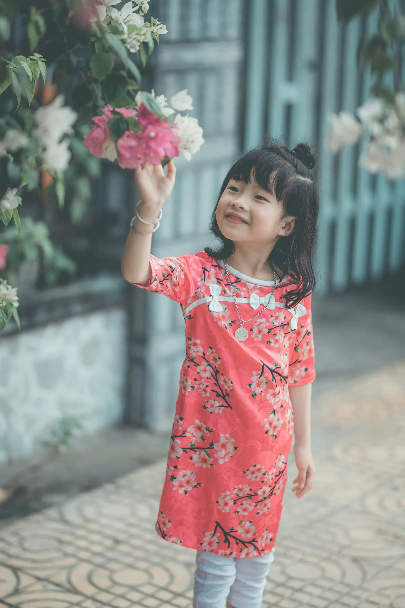 Une petite fille en robe rose sourit en touchant des fleurs de bougainvillier