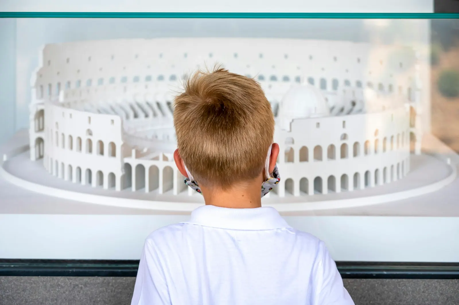 Un petit garçon, de dos, regarde une maquette blanche du Colisée à Rome