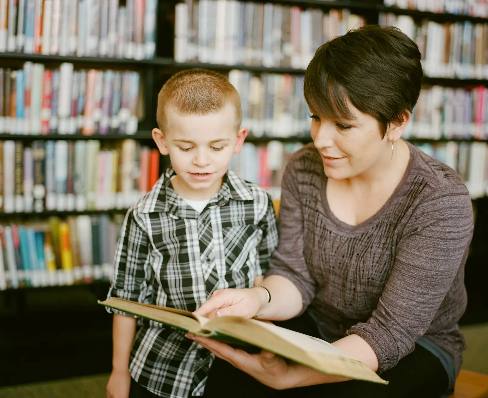 Une femme et un petit garçon lisent un grand livre ensemble dans une bibliothèque