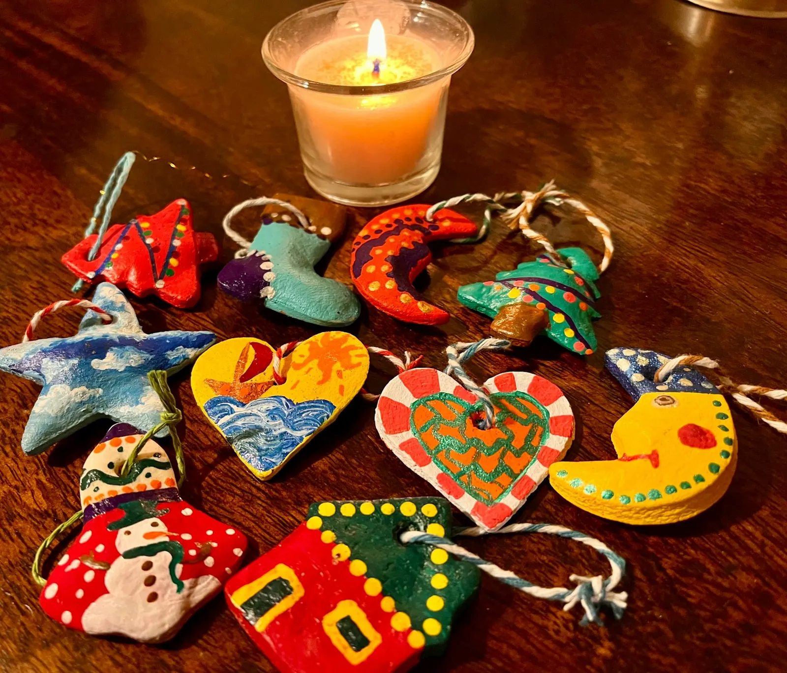 Étoile, sapin, cœur, botte et bonhomme de neige en pâte à sel peints de couleurs vives, posés sur une table en bois