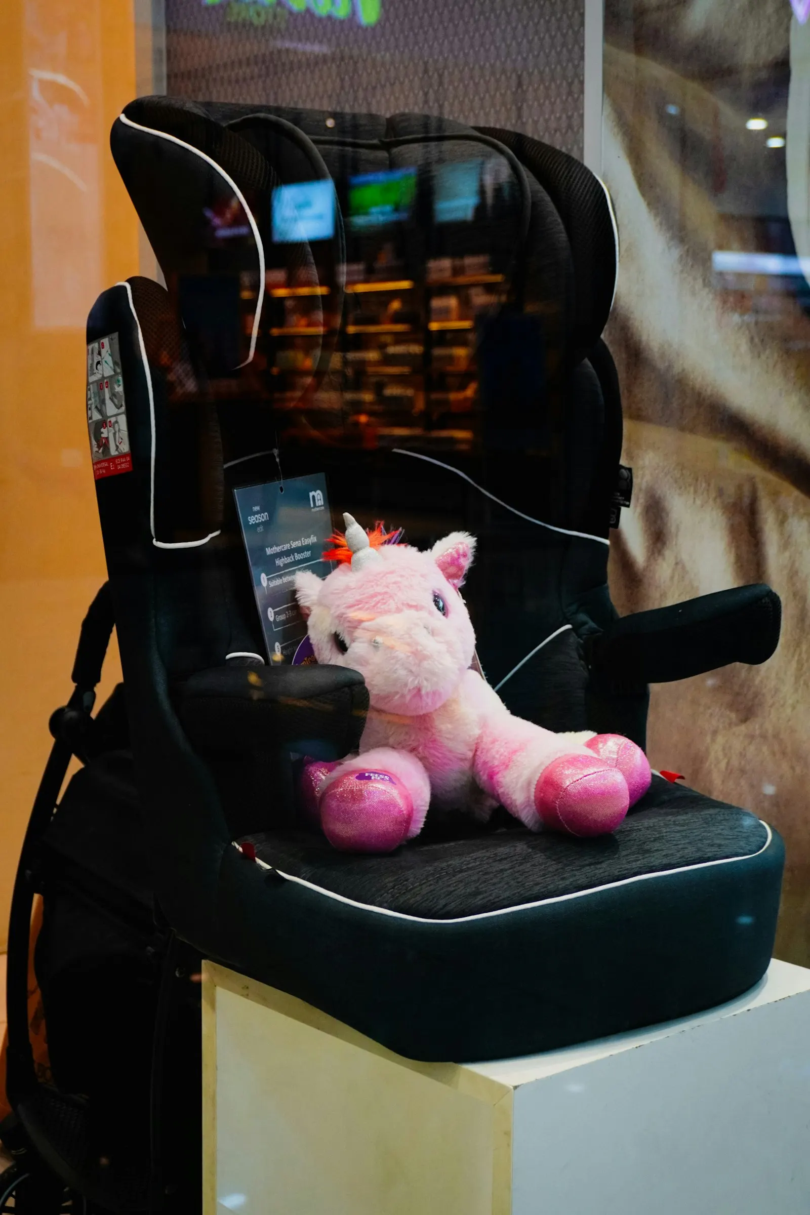 Un siège auto rehausseur noir avec une licorne en peluche posée dessus