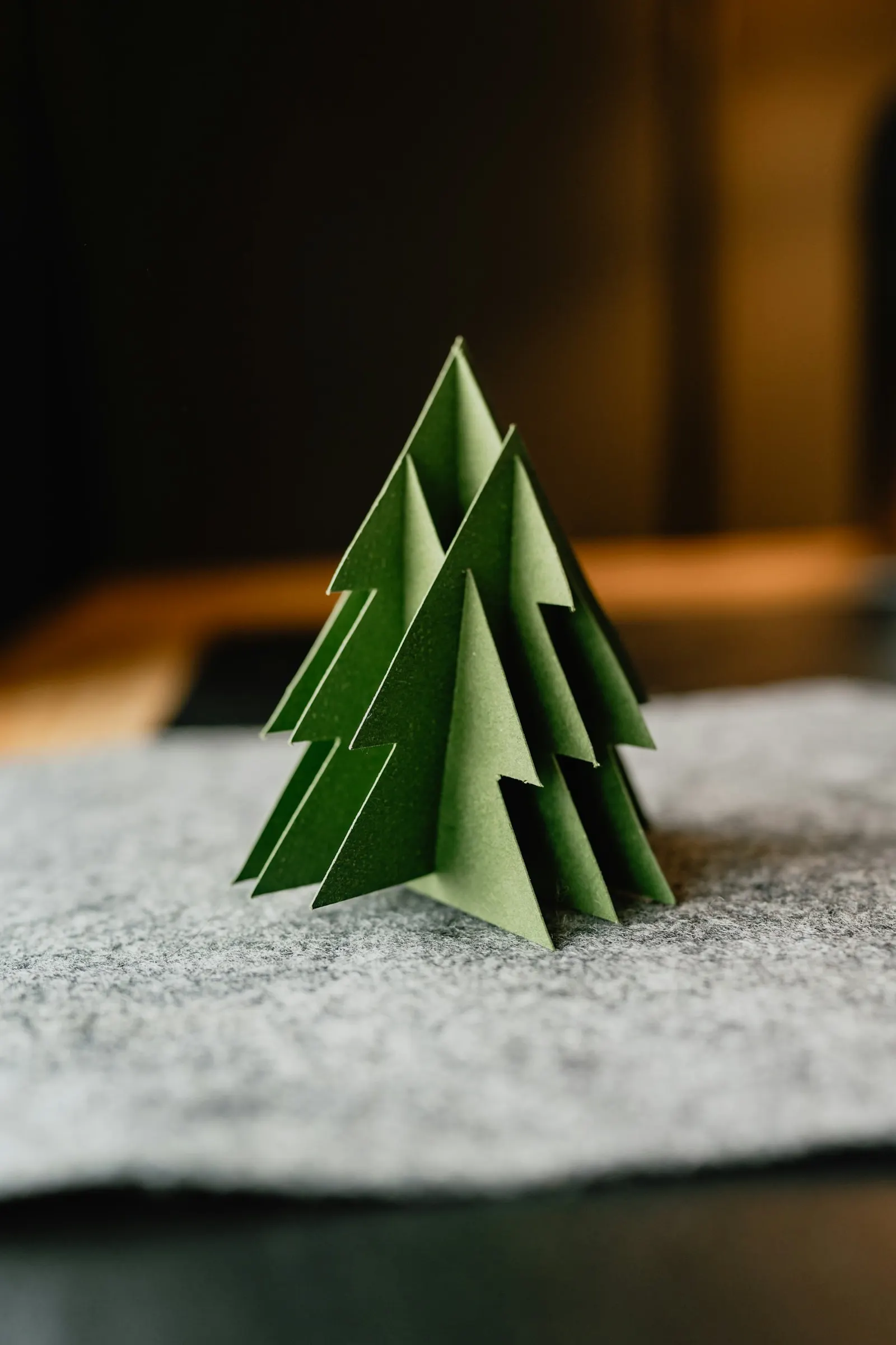 Un petit sapin de Noël en papier vert, fait de plusieurs triangles pliés, posé sur un feutre gris